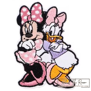 Pode incluir: Patch bordado com Minnie Mouse e Margarida. Minnie Mouse usa um laço e um vestido de bolinhas rosa, enquanto Margarida usa um laço rosa e uma blusa roxa. O patch tem um fundo branco e uma borda preta.