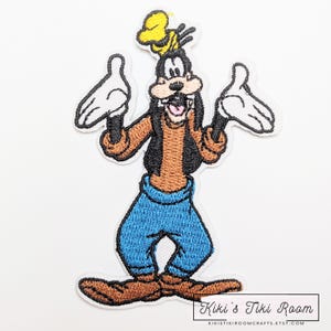 May include: Embroidered iron-on patch featuring Goofy from Disney. Goofy is wearing a brown shirt, blue pants, and a yellow hat. He is smiling and has his arms outstretched.