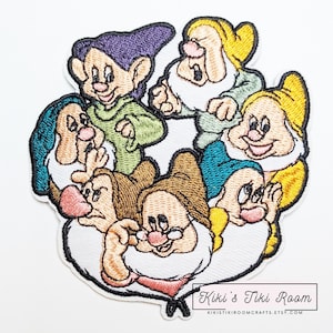 May include: Embroidered patch depicting the seven dwarfs from Snow White. The patch features the dwarfs in various colours, including purple, green, brown, and yellow, each with a distinct expression. The patch has a white border and the text "Kiki's Tiki Room" is visible.