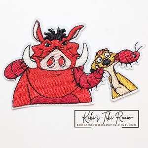 Puede incluir: Un parche bordado que muestra un facóquero rojo con colmillos blancos y pelo negro, sosteniendo una suricata de color canela que come un insecto rojo. El parche tiene un borde blanco. Debajo está el texto Kiki's Tiki Room KIKISTIKIROOMCRAFTS.ETSY.COM.
