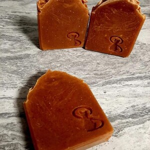 May include: Three bars of brown soap with a swirl pattern and a logo on each bar.