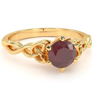 May include: A gold ring featuring a Celtic knot design and a red gemstone at its centre.