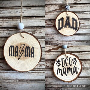 May include: Three round wooden ornaments with bark edges, each hanging from a string with a bead. One features the text MA⚡MA, another displays the word DAD in a varsity font, and the third shows the text DOG mama with two paw print icons.