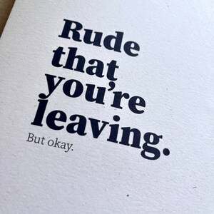 May include: A white card with the text "Rude that you're leaving. But okay." printed in a bold, black font. The card has a textured surface and a minimalist design, suitable for various occasions.