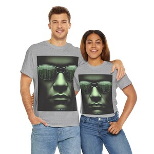 May include: Two people wearing grey t-shirts. Each shirt features a close-up of a face wearing sunglasses with a green matrix-style reflection. The text "THE ONE" is below the image. Both are wearing blue jeans.