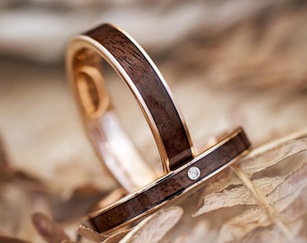 May include: Two wedding bands made of wood and rose gold. The band on top has a small diamond set in the metal.