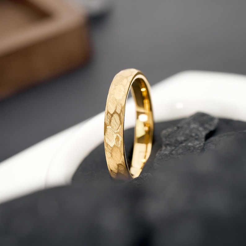 May include: A gold ring with a textured surface. The ring has a honeycomb pattern and is set against a dark background. The ring is a piece of jewelry.