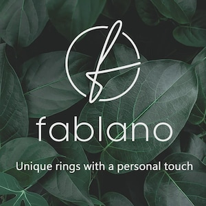 May include: The Fablano logo, a white stylized 'f' within a circle, is set against a backdrop of lush green leaves. Below, the brand name 'fablano' is displayed in white, with the tagline 'Unique rings with a personal touch'.