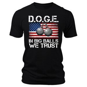 May include: Black t-shirt with a white graphic of an American flag with two weightlifting balls hanging from it. The text "D.O.G.E. In Big Balls We Trust" is printed below the flag.