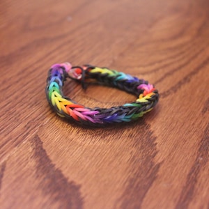 May include: A rainbow loom bracelet made with black rubber bands. The bracelet is made using a fishtail pattern.