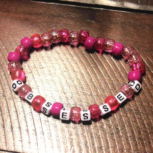 May include: Pink and white beaded bracelet with the word "BOSSED" spelled out in white letters.
