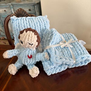 Peut inclure: Ensemble de b&eacute;b&eacute; en peluche bleu clair fait &agrave; la main, comprenant une couverture, un oreiller et une poup&eacute;e ange. La poup&eacute;e ange a des cheveux bruns, les yeux ferm&eacute;s et un c&oelig;ur rouge. La couverture est nou&eacute;e avec un ruban blanc.