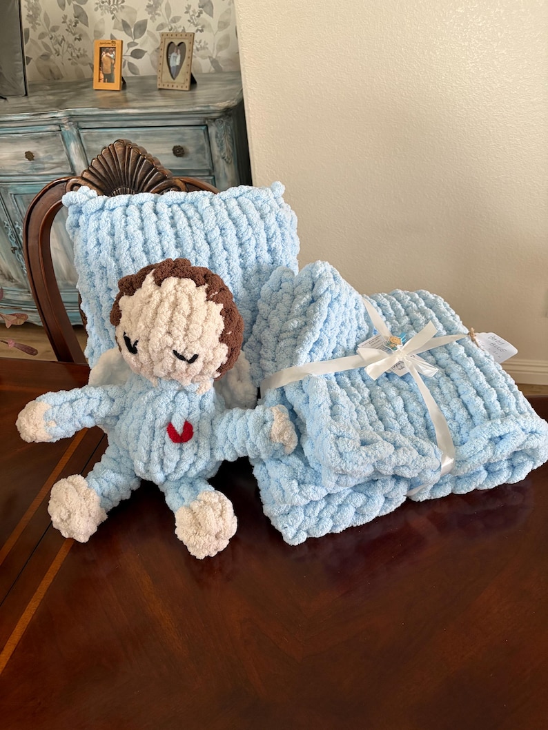 Peut inclure: Ensemble de b&eacute;b&eacute; en peluche bleu clair fait &agrave; la main, comprenant une couverture, un oreiller et une poup&eacute;e ange. La poup&eacute;e ange a des cheveux bruns, les yeux ferm&eacute;s et un c&oelig;ur rouge. La couverture est nou&eacute;e avec un ruban blanc.