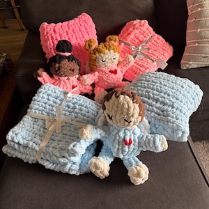 Peut inclure: Ensemble de poup&eacute;es et couvertures crochet&eacute;es &agrave; la main, roses et bleues. Les poup&eacute;es ont diff&eacute;rentes couleurs de peau et de cheveux, avec des d&eacute;tails en forme de c&oelig;ur. Les couvertures sont douces et textur&eacute;es, nou&eacute;es avec des rubans, pour b&eacute;b&eacute;.