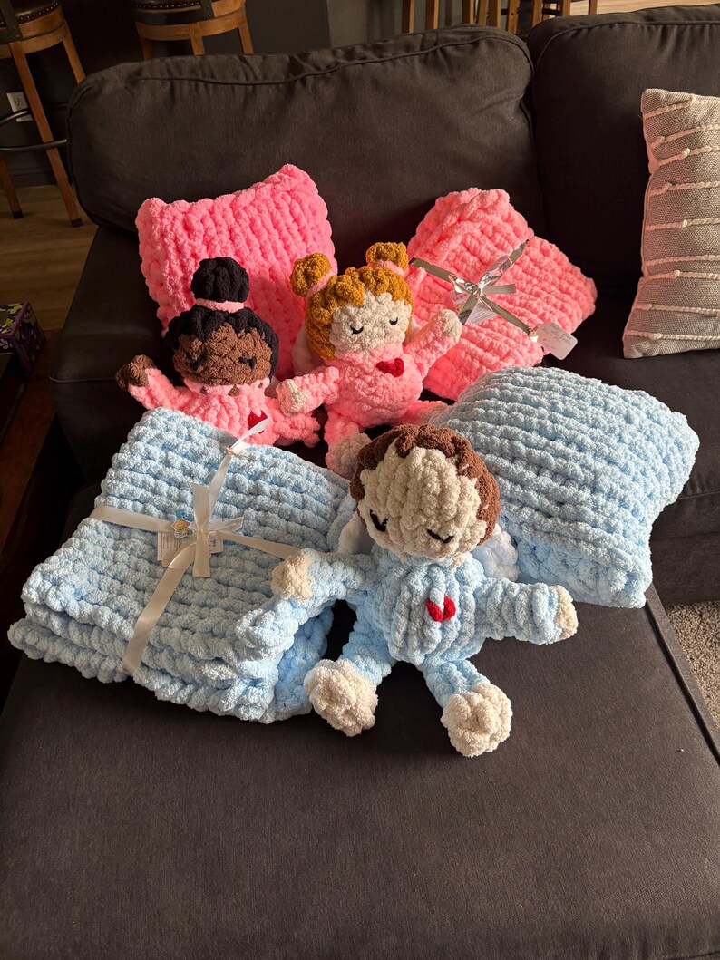 Peut inclure: Ensemble de poup&eacute;es et couvertures crochet&eacute;es &agrave; la main, roses et bleues. Les poup&eacute;es ont diff&eacute;rentes couleurs de peau et de cheveux, avec des d&eacute;tails en forme de c&oelig;ur. Les couvertures sont douces et textur&eacute;es, nou&eacute;es avec des rubans, pour b&eacute;b&eacute;.