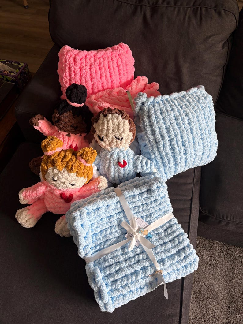 Peut inclure: Ensemble d'articles faits &agrave; la main au crochet, comprenant des coussins et des couvertures roses et bleus. Plusieurs petites poup&eacute;es au crochet avec diff&eacute;rentes couleurs de peau et de cheveux sont &eacute;galement pr&eacute;sentes, chacune avec un c&oelig;ur rouge.