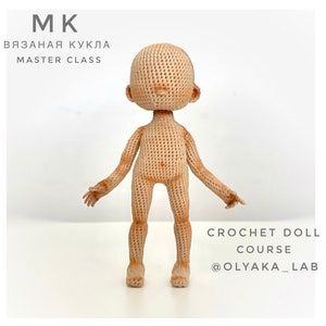 Puede incluir: Una muñeca de crochet de color nude, de pie sobre una superficie blanca. La muñeca tiene un diseño simple sin rasgos faciales. El texto "CROCHET DOLL COURSE @OLYAKA_LAB" está escrito debajo de la muñeca.