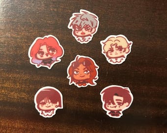 May include: Six anime-style stickers with portraits of characters with different hair colours and expressions. The stickers have a white border and are arranged on a dark brown surface.