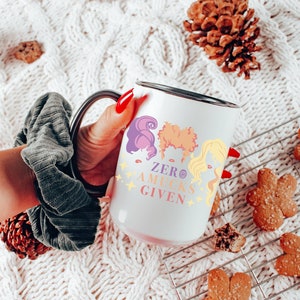 May include: White ceramic mug with a black rim and handle. The mug features a colorful illustration of three women with the text "Zero Aucks Given".