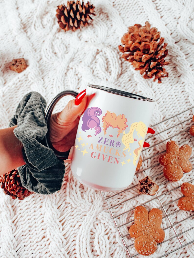 May include: White ceramic mug with a black rim and handle. The mug features a colorful illustration of three women with the text "Zero Aucks Given".