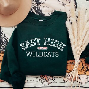 May include: A dark green sweatshirt with white text that reads "East High Wildcats" and a small red tag that says "Est. 2006".