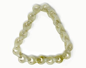 Puede incluir: Un brazalete de cadena translúcida verde claro. Los eslabones tienen forma ovalada con una apariencia texturizada y moteada. El brazalete está dispuesto en forma triangular sobre un fondo blanco.