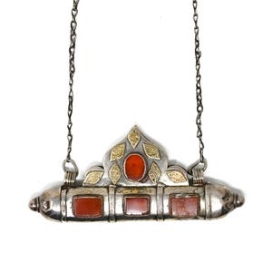 May include: Silver-toned pendant necklace with a decorative design. The pendant features three rectangular red stones and a central oval red stone, accented with gold-colored leaf-like details. The necklace hangs from a delicate chain.