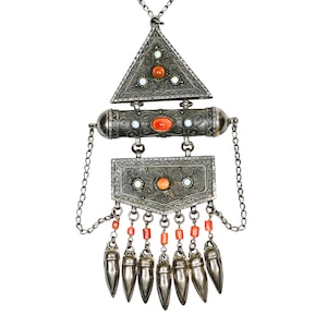 May include: A silver pendant featuring a triangular top, a cylindrical middle section, and a rectangular base, all decorated with intricate filigree patterns. The piece is inlaid with orange and white stones and includes seven dangling silver charms.