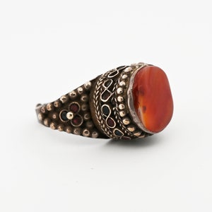 May include: A silver ring with a large, oval-shaped carnelian stone set in a bezel. The ring is decorated with intricate silver filigree and small red and blue stones.