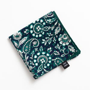 May include: A folded navy blue and teal paisley patterned handkerchief with a dark green border. The handkerchief has a white floral design. A small black tag with the text "CHIEF HANKS" is attached to the corner.