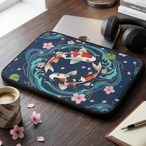 Puede incluir: Una funda para portátil azul marino con un diseño de peces koi. El diseño incluye dos peces koi, flores de cerezo rosas y remolinos de agua azules. La funda tiene un borde negro y está sobre un escritorio de madera.