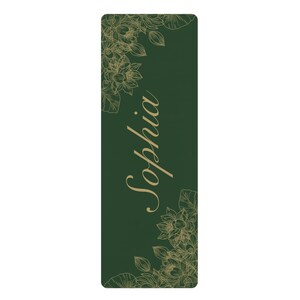 May include: A rectangular dark green yoga mat featuring a gold-colored line art illustration of lotus flowers in the top left and bottom right corners. The name Sophia is printed in a large, elegant gold-colored script font in the center.
