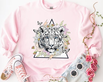 May include: A pink sweatshirt with a graphic print of a white snow leopard's face surrounded by flowers and butterflies inside a black triangle.
