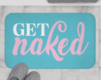 Pode incluir: Um tapete de banho retangular turquesa com as palavras "GET naked" em branco e rosa. Chinelos cinzentos estão na parte inferior esquerda. Uma toalha cinzenta está no topo.
