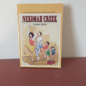 May include: A yellow book cover with the title "Nekoma Creek" by Linda Crew. The cover features an illustration of a family dancing to music from a record player.