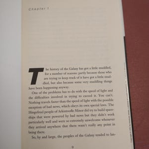 Puede incluir: Un libro con una cubierta blanca y texto negro. El t&iacute;tulo del libro es "Cap&iacute;tulo 1". El texto de la p&aacute;gina trata sobre la historia de la Galaxia y la velocidad de la luz.