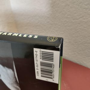 Puede incluir: Un libro negro de tapa dura con el t&iacute;tulo "HARMLESS" en la portada. El libro tiene un c&oacute;digo de barras y un n&uacute;mero ISBN en la contraportada. El n&uacute;mero ISBN es 0-517-57740-2.