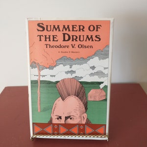 May include: A vintage paperback book titled "Summer of the Drums" by Theodore V. Olsen. The book cover features a cartoon illustration of a Native American man with a mohawk hairstyle, a small cabin, and a green landscape.