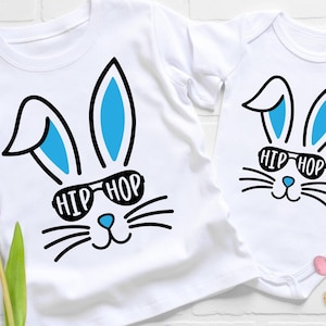 May include: Two white t-shirts featuring a blue and black bunny rabbit design. The bunny is wearing sunglasses that say "Hip Hop".