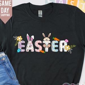 Op de afbeelding: Zwart T-shirt met een kleurrijke paasafbeelding met konijnen en het woord "Easter" in een speels lettertype.