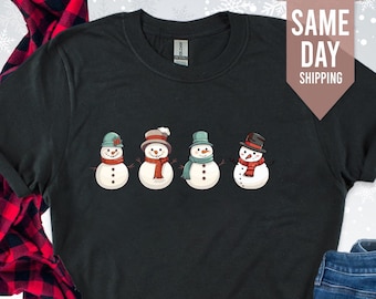 May include: Black t-shirt with a graphic of four snowmen wearing hats and scarves. The text "SAME DAY SHIPPING" is in the top right corner of the image.
