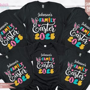 Op de afbeelding: Vijf zwarte T-shirts met een wit grafisch ontwerp met de tekst "Johnson's Family Easter 2025" met kleurrijke konijnenoren, harten en cijfers.