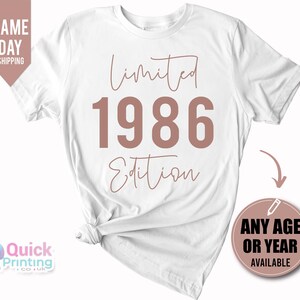 May include: A white short-sleeved t-shirt featuring the text Limited Edition in a cursive script font with the year 1986 printed in large, bold, dusty rose-colored block lettering centered on the front of the garment.