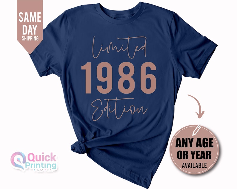 May include: A navy blue short-sleeved t-shirt featuring the text "Limited 1986 Edition" in a light pink color. The word "Limited" and "Edition" are written in a cursive script font, while the numbers "1986" are in a bold, block-style font.