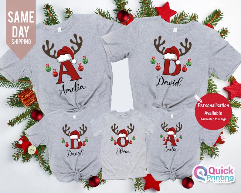May include: A collection of gray Christmas t-shirts with reindeer antlers, Santa hats, and personalized letters and names. The shirts are decorated with red and green ornaments. The text "Amelia", "David", and "Olivia" are visible.
