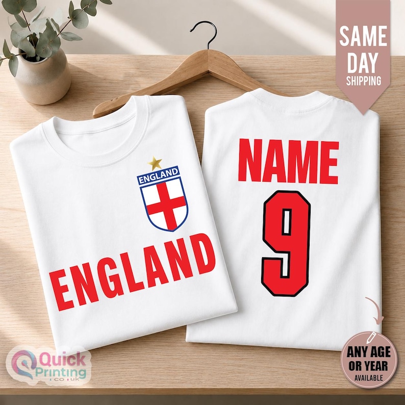 May include: Two white t-shirts featuring red text and graphics. The front shirt displays the word ENGLAND in red with a blue and white England crest above it. The back shirt shows the word NAME in red above the large red number 9.