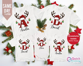 Pode incluir: Camisetas brancas de Natal para a família com chifres de rena, gorros de Papai Noel e nomes personalizados. Cada camiseta apresenta uma letra e um nome, com enfeites vermelhos e verdes. A imagem também inclui o texto "SAME DAY SHIPPING".