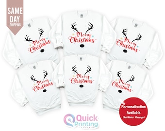 May include: White Christmas sweatshirts with a reindeer face design. The design includes black antlers, a black nose, and the words "Merry Christmas" in red script. The sweatshirts are long-sleeved.