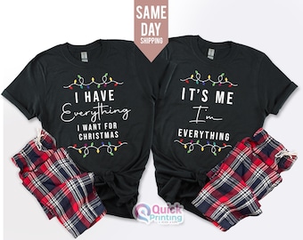 Könnte beinhalten: Zwei schwarze T-Shirts mit Weihnachtslichtern und Text. Das erste Shirt sagt "Ich habe alles, was ich zu Weihnachten möchte". Das zweite Shirt sagt "Ich bin es, ich bin alles".