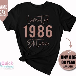 May include: A black short-sleeve t-shirt featuring the text Limited Edition in a cursive font with the year 1986 in a large bold sans-serif font in the center. The text is printed in a muted rose gold color on the front of the garment.